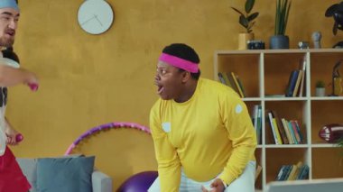 Canlı bir oturma odasında, iki erkek spor salonu ile dolu eğlenceli bir günün keyfini çıkarırken, bir kadın hulahop çalarken, halterler ve halterler arasında gidip geliyor.