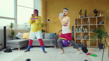 Canlı bir videoda iki erkek, bir pilates topu ve direniş bandıyla oturma odasında çalışıyor ve onlara bir kadın ve bir erkek eşlik ediyor.