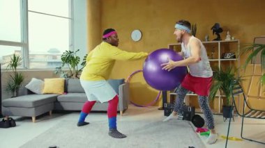 İnsanlar antrenmanlara katılırken, hareketli bir oturma odası enerjiyle uğulduyor. İki adam mor bir egzersiz topu kullanırken, birkaç koordinat egzersizi yapıyor.