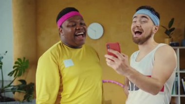 Konforlu bir oturma odasında, iki adam bir cep telefonunu tartışıyor, bir kişi hevesle görüşlerini paylaşıyor. Yoldaşlıkları teknolojilerin etkileşimlerdeki rolünü vurguluyor