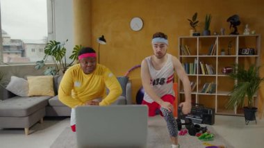 Konforlu bir oturma odasında, iki adam dizüstü bilgisayarlarındaki bir spor programını takip eder ve gücünü arttırmak için egzersiz yaparlar. Bir kadın katılıyor, dinamik enerji ekliyor.