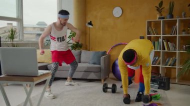 Bu video, iki adamın canlı bir oturma odasında, halterli, spor yapan ve ortaklık gösteren bir dizüstü bilgisayarla birlikte egzersiz yapmasını içeriyor.