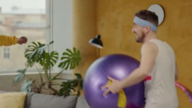 Bu video iki adamın farklı yerlerde mor bir egzersiz topunun keyfini çıkardığını gösteriyor. Bir erkek ve bir kadın da hula çemberine katılıp eğlenceyi arttırıyor.