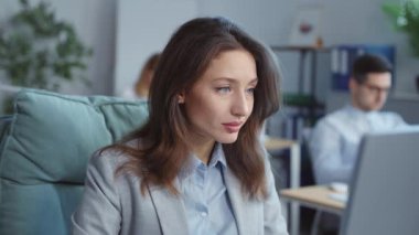 Odaklanmış çekici iş kadını ofiste dizüstü bilgisayarla çalışırken kameraya bak. Çalışan arka plandaki insanlar