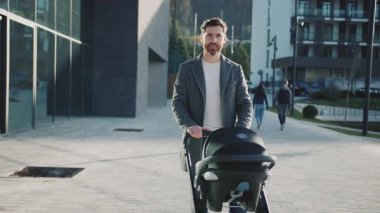 Bebek arabasında yeni doğmuş bebeğiyle portre babası kameraya bakar. Şehirde, gün ışığında caddede. Açık havada. Yavaş çekim