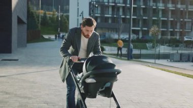 Bebek arabasında yeni doğmuş bir bebekle açık hava yakışıklısı bir baba sokakta gün ışığında çocuğu sakinleştirmeye çalışır. Yavaş çekim