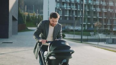 Bebek arabasında yeni doğmuş bebeğiyle komik yakışıklı bir baba gün ışığında şehir caddesinde çocuğu sakinleştirmeye çalışır. Açık havada. Yavaş çekim