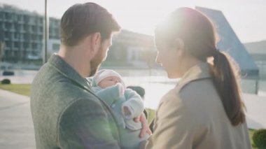 Gün batımında anne ve baba yeni doğmuş bebeği ellerinde tutarak birlikte oynuyorlar. Gülümseyen mutlu hisseder. Sokakta açık havada. Yavaş çekim
