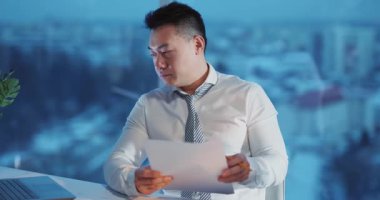 Bir işadamı, arka planda şehir görüşü olan belgeleri dikkatle inceleyerek profesyonelliği vurguluyor..
