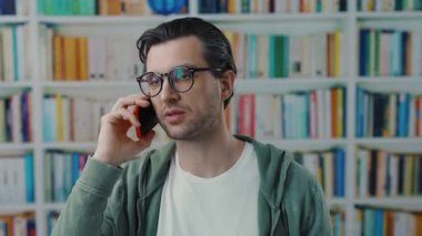 Çağdaş bir adam canlı ve renkli kitaplıklarla çevriliyken bir telefon konuşmasına daldı.