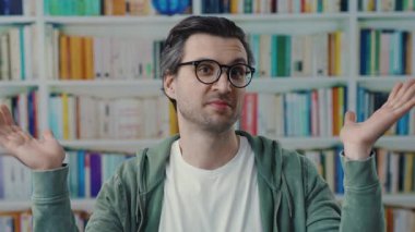 Genç bir adam canlı, renkli bir kitaplığın önünde düşünceli bir şekilde duruyor derin düşünceli bir ifadeyi sergiliyor.