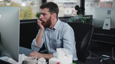 Sakallı bir adam, şık ve çağdaş bir ofis ortamında masasında özenle çalışıyor.