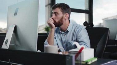 Masasında çalışmayı düşünen düşünceli bir adam modern ofis ortamını ve verimliliğini gözler önüne seriyor..
