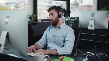 Kulaklık takan bir adam modern çalışma kültürünü temsil eden çağdaş bir ofis alanında yoğun bir şekilde yazı yazıyor.