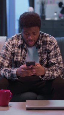 Akıllı telefonuna odaklanmış genç bir adam modern dijital yaşam tarzını rahat ve rahat bir ortamda resmediyor.