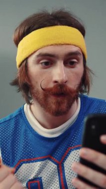 Retro spor forması ve şık bir saç bandı giyen odaklanmış bir adam akıllı telefonuyla çok meşgul.