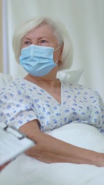 Genç doktor, yaşlı, sağlıksız bir kadının hastane odasında iyileşme sürecine girmesi için danışmanlık yapıyor. Tıbbi bir randevu. Yüz maskeleri. Coronavirüs.