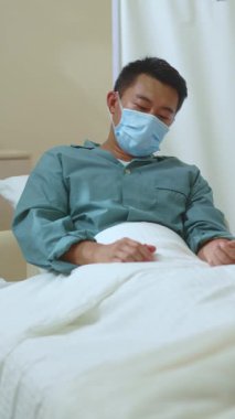 Coronavirus. Karantinaya alın. Yüzü maskeli sağlıksız sefil Çinli adam hastane yatağında öksürürken acı veren 19 semptomdan muzdarip. Grip oldum. Hastanedeyiz. Kötü durumda..
