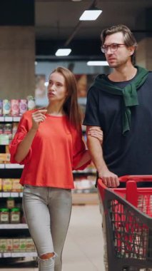 Beyaz, güzel, genç ve güzel bir aile alışveriş arabasıyla marketten alışveriş malzemeleri seçiyor. Yiyecek alışverişi. Tüketim. İletişim.