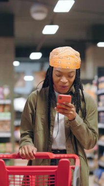 Tatmin olmuş Afro-Amerikan tarzı bir kadın çevrimiçi zafer hedeflerini kutluyor video oyunu kazanıyor alışveriş merkezindeki akıllı telefon mesajlarıyla eğleniyor..