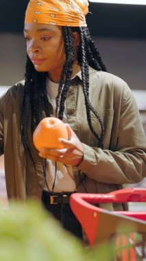 Afro-Amerikalı güzel kadın marketten meyve alıyor. Organik süpermarkette yürüyen ciddi bir stil kızı en kaliteli taze portakal meyvesini seçiyor..