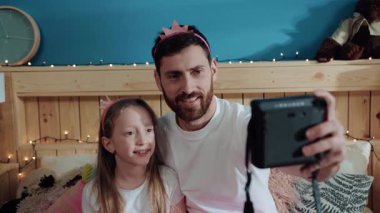 Mutlu gülümseyen baba ve kız periler gibi giyinmiş yatak odasındaki polariod fotoğraf makinesinde selfie çekiyor ve gülümsüyor. Ev partisi, aile fotoğrafı..
