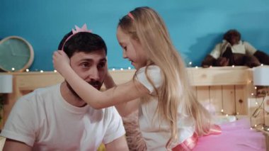 Yakından bakınca tatlı bir kız prensesin babasının kafasına taç taktığını görüyoruz. Küçük kız babasını prenses gibi giydiriyor. Kostümlü parti için..