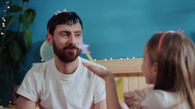 Yakından güzel bir kız sihirli bir el sallayarak babasının yüzüne kozmetik tozu üflüyor ve onu mutlu bir gülümseme perisine dönüştürüyor. ev kostümü partisi doğum günü kutlaması.