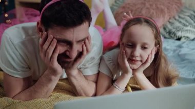 Yakın aile portresi. Neşeli komik baba ve kızı birlikte çizgi film izliyorlar. Yüksek açı manzaralı mutlu bir adam ve evde oynayan periler gibi giyinmiş küçük bir kız..