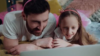 Sevimli bir portre, baba-kız yatak odasında dizüstü bilgisayardan video izliyor. Pembe elbiseli komik genç adam ve kız özel parti kutlamalarında perilik oynuyorlar..