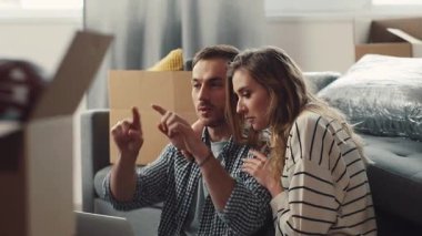 Genç bir çift, rahat bir yaşam alanındaki kutuların taşındığı bir dizüstü bilgisayarda ortak bir görev üstlendi.