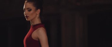 Çarpıcı kırmızı kıyafetli yetenekli bir dansçı sahnede zarif bir şekilde poz verir. Yoğun ve dramatik ışıklandırmayla aydınlatılır.