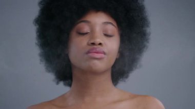 Bir kuaförde makyaj yaptıktan sonra yüzüne su serpiştiren güzel Afro-Amerikalı zenci kadın portresi. Çekici bir kadının yüz bakımını üstlendiği yakın çekim. Kameraya bakıyor..