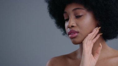 Makyaja hazırlanırken yüzüne nazikçe dokunan güzel Afro-Amerikan kadının yakın çekimi. Temiz, doğal ciltli ve kameraya bakan güzel bir genç bayanın portresi..