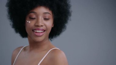 Gri arka planda kameraya gülümseyen iç çamaşırlı çekici siyahi genç bayanın muhteşem portresi. Harika kıvırcık saçlı Afrikalı kız içeride eğleniyor..