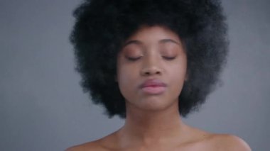 Profesyonel makyaj prosedüründen önce yüzüne nemlendirici sprey sıkan güzel Afrikalı Amerikalı kadının yakın plan portresi. Güzel kıvırcık saçlı siyah kız, karanlık arka planda izole edilmiş..