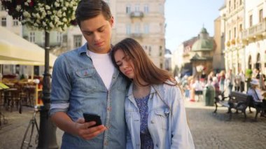 Genç, üzgün, aşık bir çift cep telefonuna bakıyor. Kafenin arka planında kız arkadaşına sarılan yakışıklı bir genç. Haberler kötü. Şehir merkezinde. Yaz zamanı. Açık havada..
