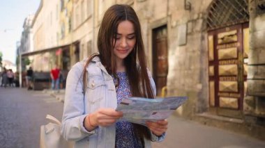 Güzel kahverengi saçlı, sokakta yürüyen sevimli, gülümseyen Ukraynalı turist. Kayıp güzel kız haritayı elinde tutuyor, etrafa bakıyor. Yaz zamanı. Açık havada.
