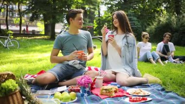 Güzel bir parkta çimlerin üzerinde oturan mutlu beyaz bir çift. Bisikletlerin arka planında içki içip yemek yiyen genç iyi görünümlü insanlar. Yaz zamanı. Piknik. Açık havada..
