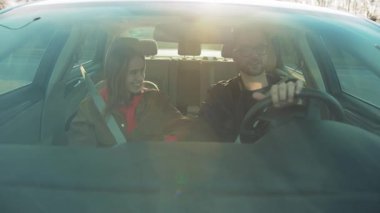 Genç bir adam ve bir kadın birlikte keyifli bir yolculuk paylaşıyorlar, güzel bir şekilde arabanın ön panelinden görüntülenmişler.