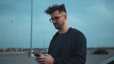 Şık bir genç adam akıllı telefonuyla, şehir manzarasında modern bir hava yakalıyor.