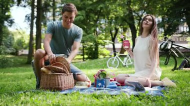 Genç çift parkta dinleniyor, piknik yapıyor, içki içiyor, egzotik meyve kadını, kitap okuyor, aşk kadını, yaz aşkı doğası, duygusal, dışarı çıkıyor, keyif alıyor, yavaş çekim yapıyor.