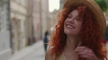 Genç, gülümseyen, kızıl saçlı, kameraya bakan, şehirde yürüyen mutlu, yavaş çekim yaz yüzleri teknolojisi, Kafkasyalı, güzel, açık hava kadın portresi, sevimli duygular.