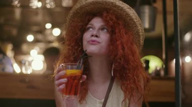 Tarz sahibi, genç, çekici, şapkalı, kırmızı saçlı bir kadın kafede oturmuş içki içiyor. Moda kızı bağlantısı kuruyor. Kafkasyalı akıllı telefonlu kadın, yavaş çekim çekimini kapatıyor.