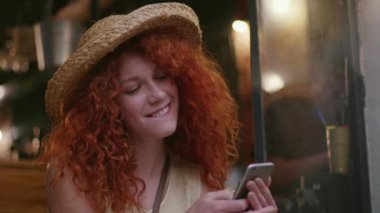 Kafede oturan, şapkalı, genç, çekici bir kadın. Moda kızı bağlantısını kullan. Yazın, beyaz, akıllı telefonlu genç bayan.