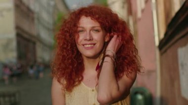 NEW YORK - 5 Nisan 2017: Kırmızı kıvırcık saçlı mutlu genç kadın, şehrin sokaklarında yürürken kameraya bak yavaş çekim yaz portresi, günlük beyaz gün batımı güzel bayan.