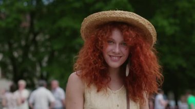 Kırmızı kıvırcık saçlı genç kadın kameraya bak, gülümse, sokaklarda gülümse, yavaş çekimde gülümse, yaz yüzlü, beyaz tenli, güzel bayan dış görünüşlü, şirin.