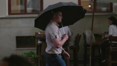 Ciddi, genç ve çekici bir adam şemsiyeli su siluetiyle sokakta yürüyor. Beyaz, duygusal, ağır çekimde yaz portresi.