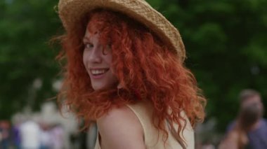 Kırmızı kıvırcık saçlı güzel bir kadın kameraya bakıp gülümse. Mutlu bir şekilde şehir sokaklarında yürü. Yazın Kafkas günbatımında yüz yüze gel.