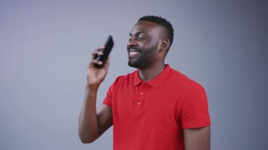 Yakışıklı genç Afro-Amerikalı adam telefonu kapatıyor, kameraya bakıyor, gri arka planda mutlu bir şekilde gülümsüyor. Neşeli ruh hali, olumlu duygular, mutlu olmak. Erkek portresi, yakın görünüm